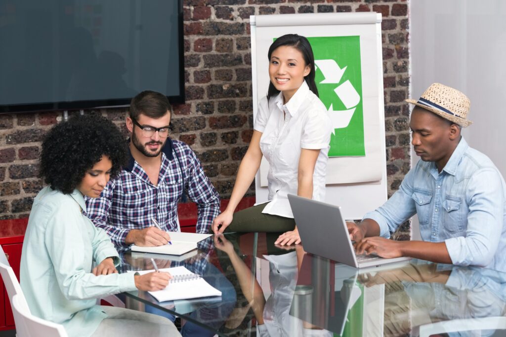 Workplace team in a meeting writing or typing notes with woman leading meeting about recycling