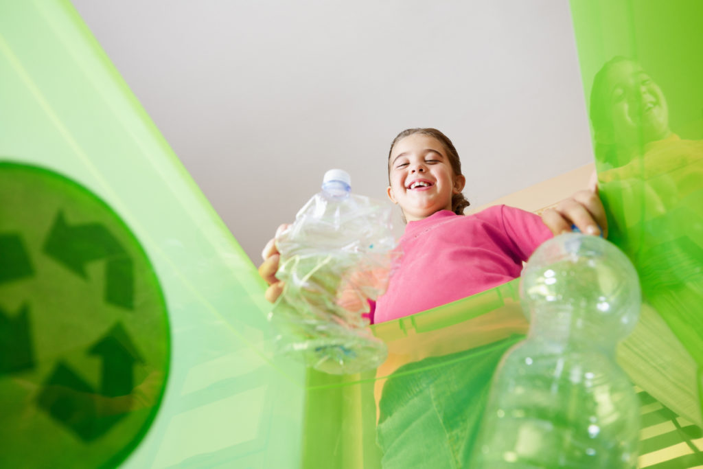 Girl holding plastic bottles for recycling, viewed from inside recycling bin. 