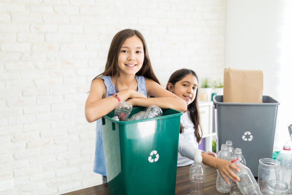 Portrait of confident preteen girl gathering bottles with sister at home