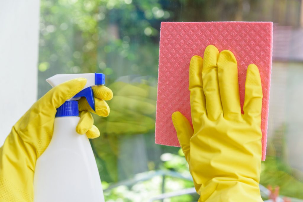 Cleaning of closed vinyl plastic window. Protective yellow gloves on hands and cleaning cloth with sprinkle