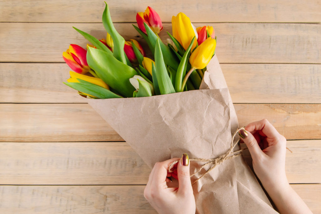 The process of wrapping bouquet of fresh tulips in eco-friendly craft paper. 