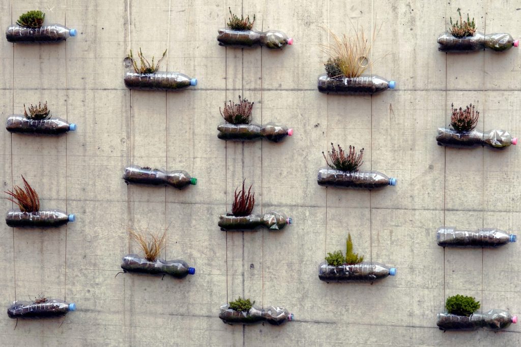 Do it yourself garden of up-cycled plastic bottles are alternative flower pots. Bottles are fixed with strings on concrete wall.