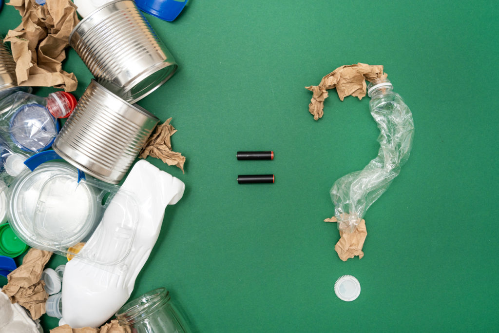 Different types of garbage paper, plastic, metal and other assorted waste in composition with question mark made of trash isolated on green background. 