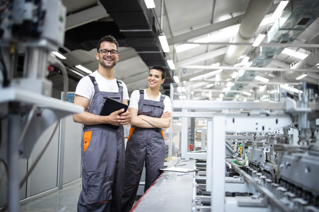 Portrait of production line workers controlling manufacturing process of modern packaging industrial machine in printing factory.