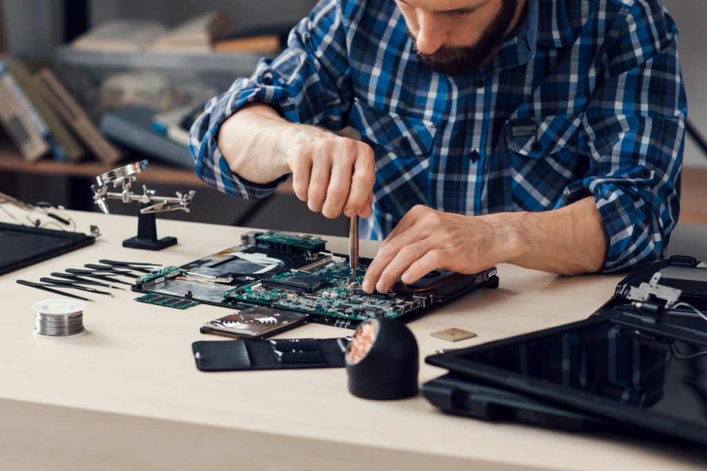 Laptop disassembling with screwdriver at repair shop. Engineer fixing broken computer motherboard in order to recycle old electronics