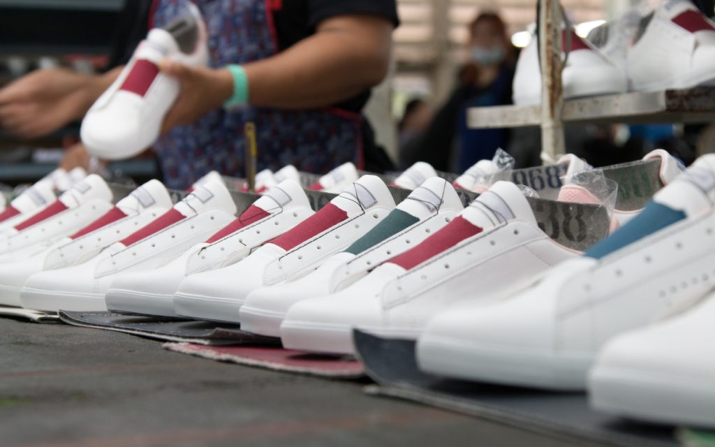 worker making white leather shoe on production line conveyor in footwear factory