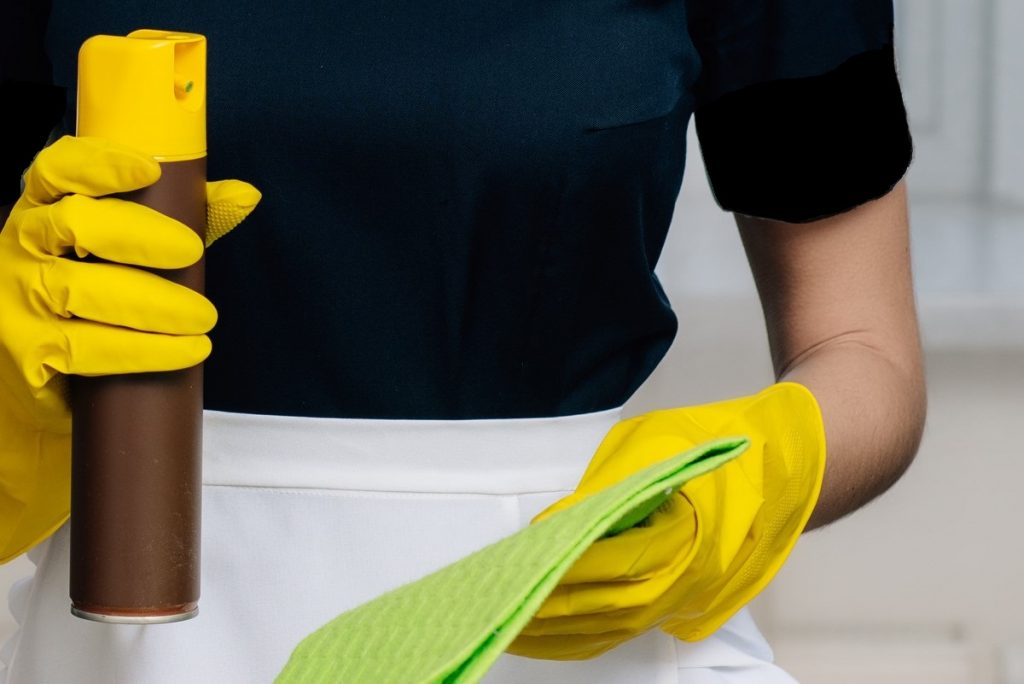 Someone wearing rubber gloves about to spray cleaning product from an aerosol can into a cloth