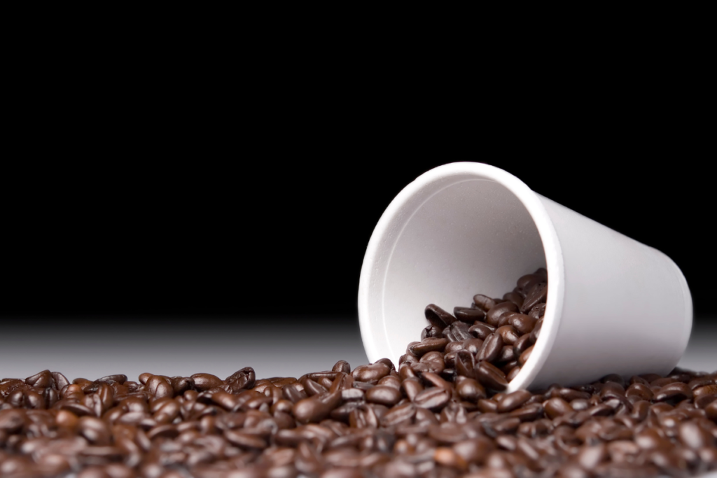 Styrofoam disposable coffee cup tipped on its side with coffee beans spilling out