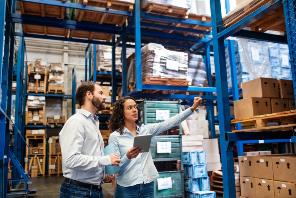 Businesswoman with a tablet showing the male worker in distribution area and talking to him. Warehouse full of inventory in the background