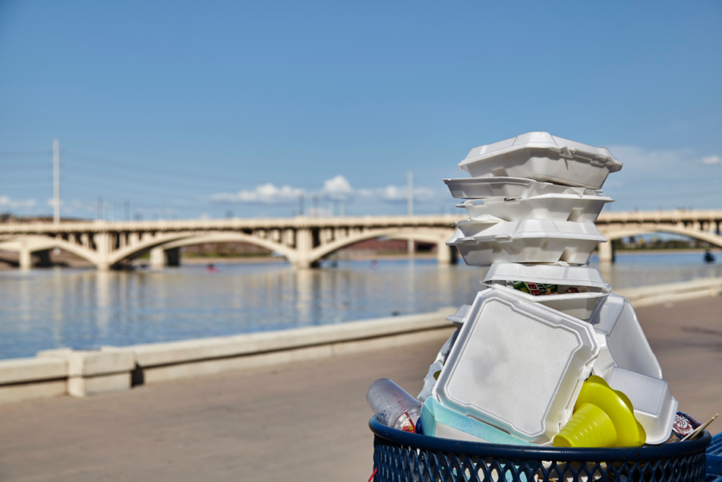 Styrofoam containers stacked high in a garbage can next to a river